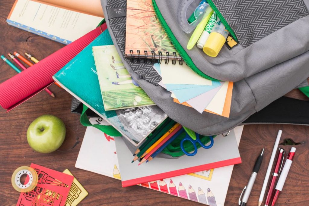 Open school backpack with books, notebooks, and supplies on a wooden table
