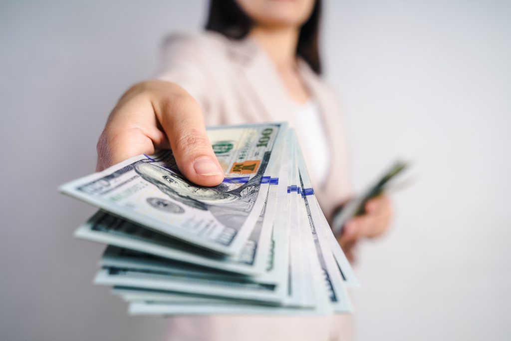 Close-up of a businesswoman’s hands holding out US dollar bills toward the camera.