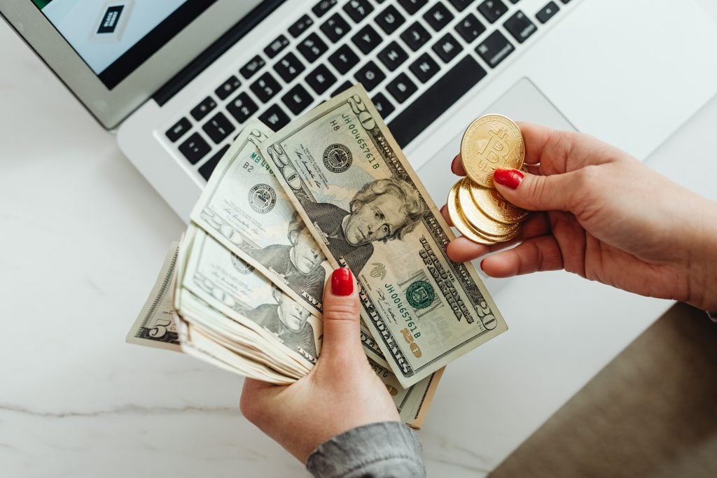 Close-up of a hand flipping through a stack of 100-dollar bills on a white background.