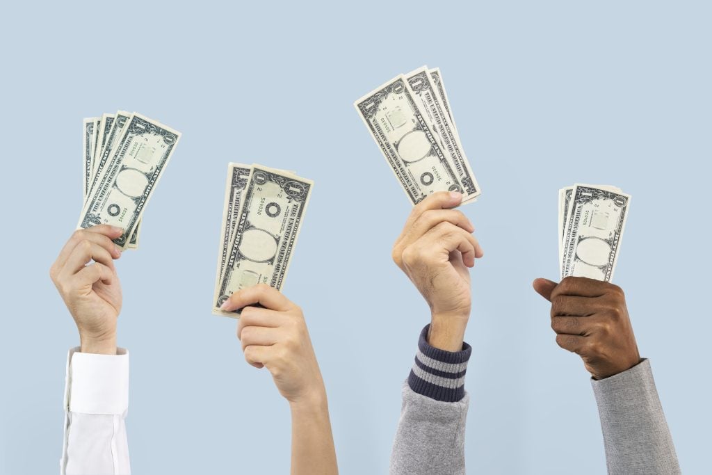 Silver bitcoin coins placed on top of 100-dollar bills in a close-up finance concept image.